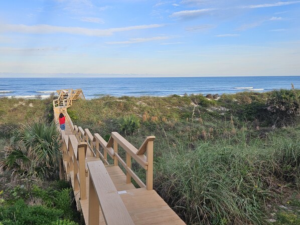A wooden boardwalk leading to the beach with a person in a red shirt walking away.