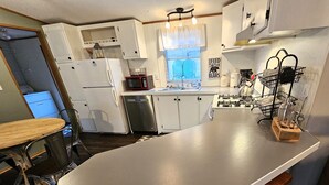 Een keuken met witte kastjes, een RVS vaatwasser, een magnetron, een gasfornuis en een houten bankje.