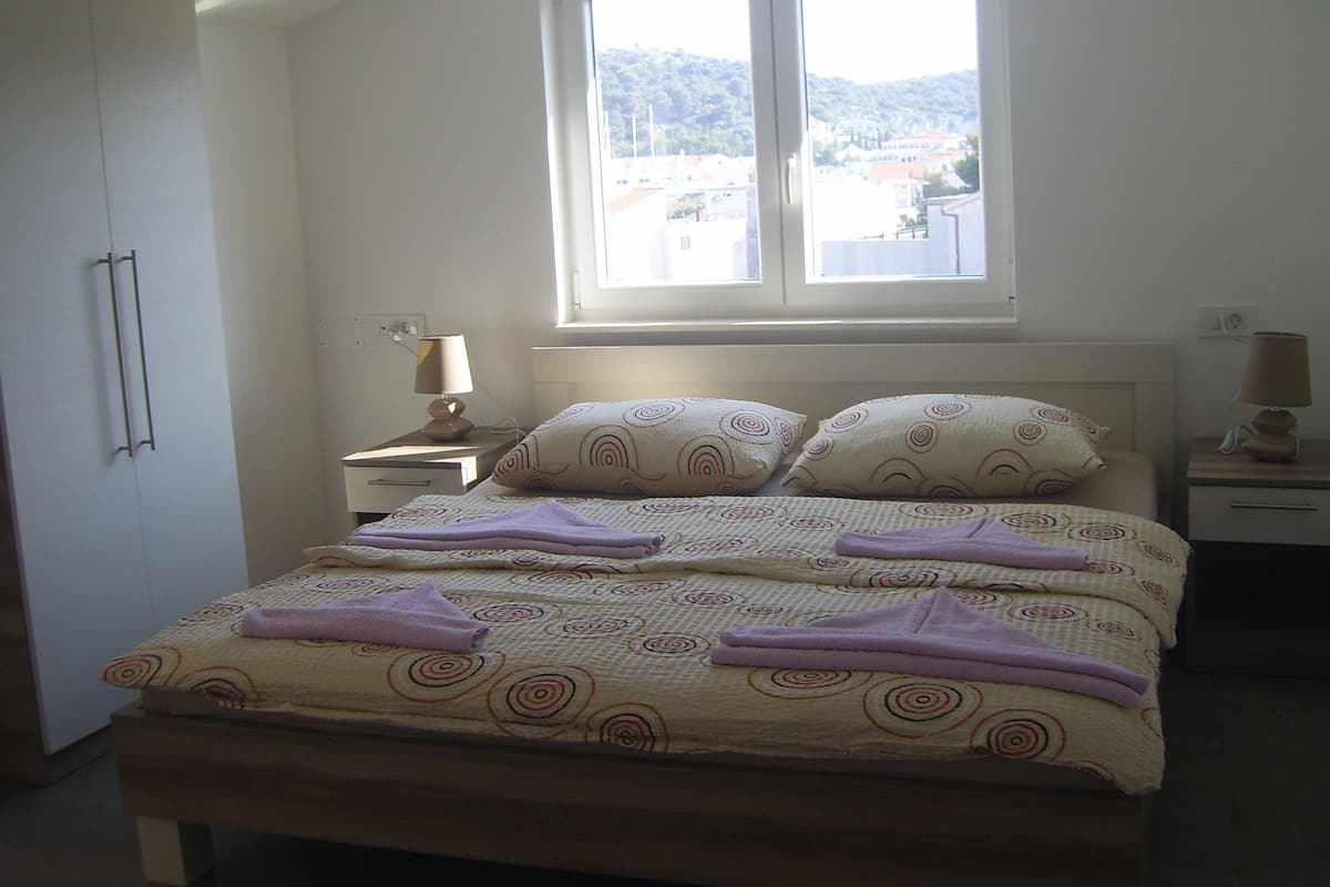 A bedroom with a bed, two bedside tables, a window, and a wardrobe.