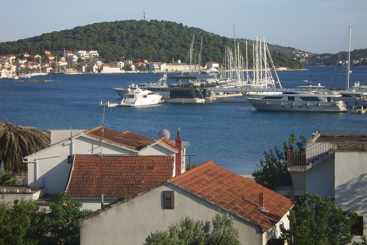 A marina with several yachts docked, surrounded by residential buildings and a hill in the background.