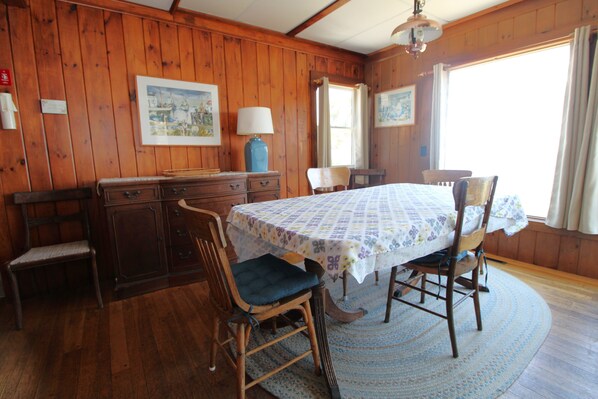 A wooden room with a dining table, chairs, a lamp, and artwork on the walls. - Cottage with Views of the Atlantic Ocean (1221) (Wellfleet)