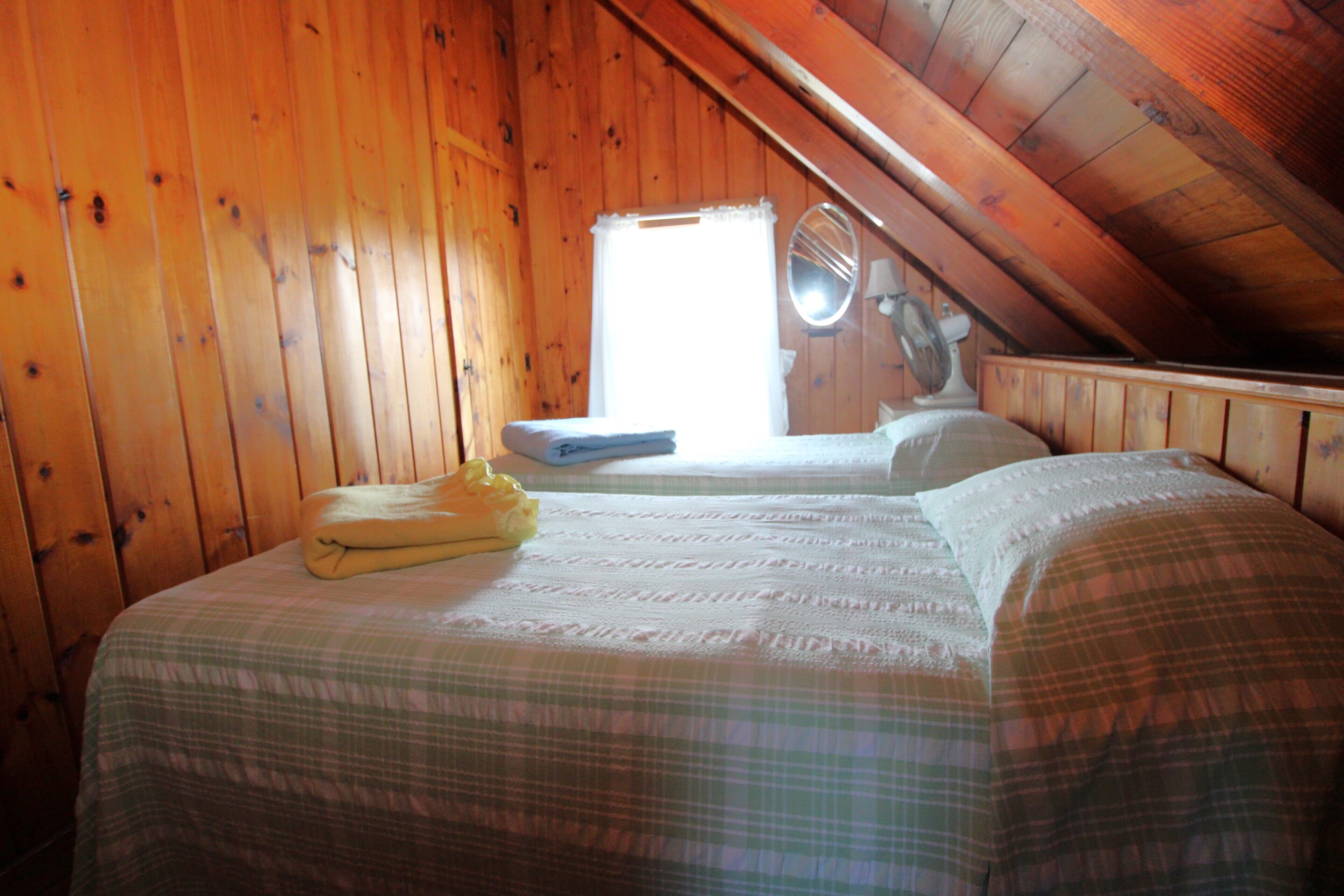 Um quarto de sótão acolhedor, com paredes de madeira, uma cama com roupa de cama xadrez e uma pequena janela com espelho.
