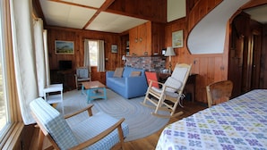 Un acogedor interior de cabaña con un sofá azul, sillones mecedores, una mesita y una chimenea.