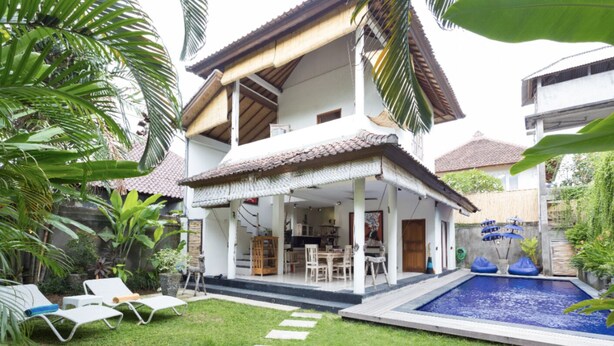 Una casa de dos pisos con un porche cubierto, piscina y un césped bien cuidado.