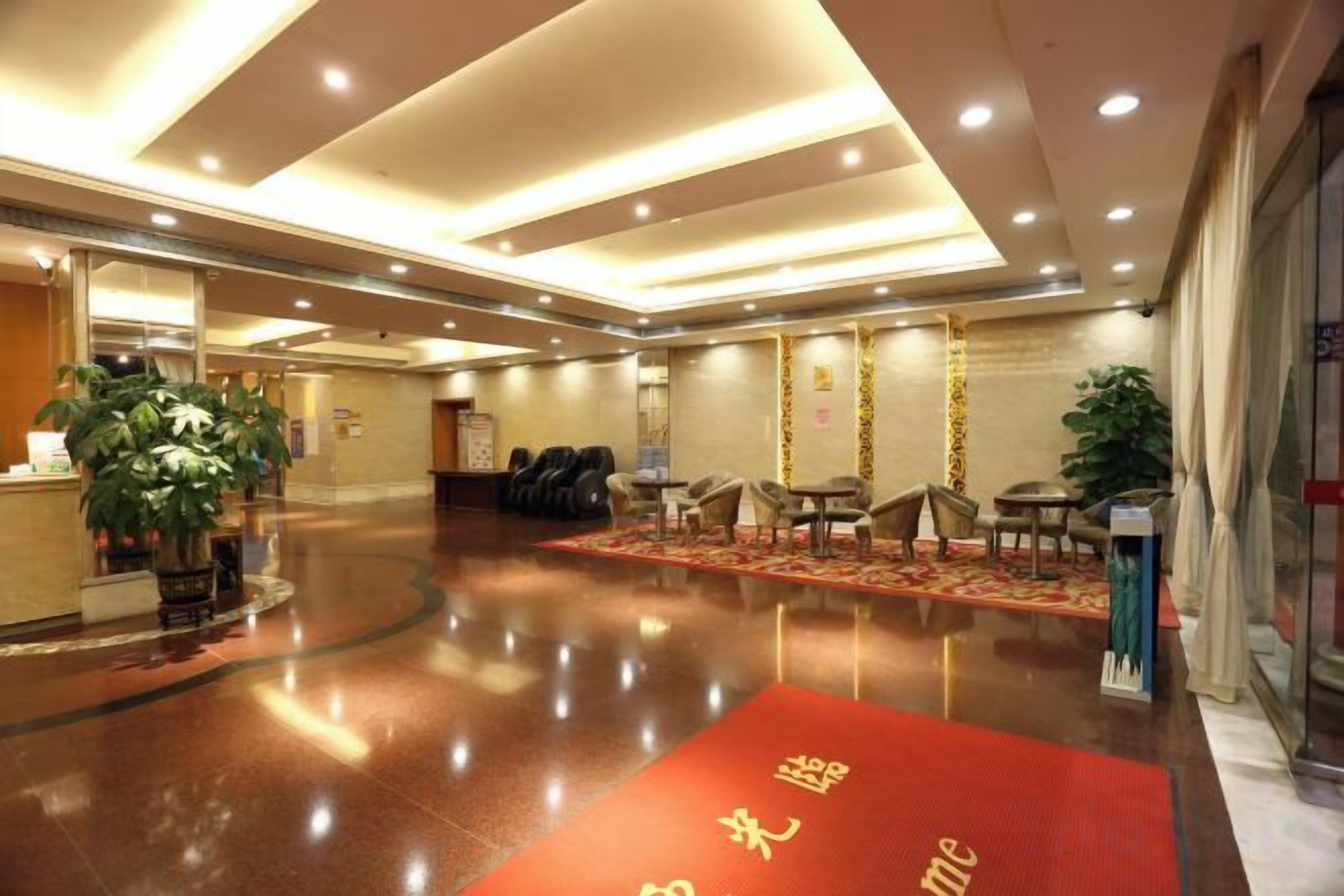Un vestíbulo de hotel con una recepción, área de descanso y una alfombra roja con letras doradas.