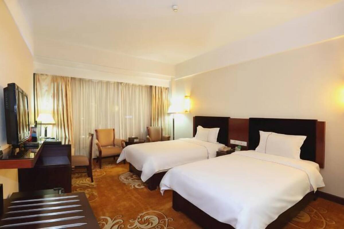 A hotel room with two beds, a desk, a chair, and a TV.