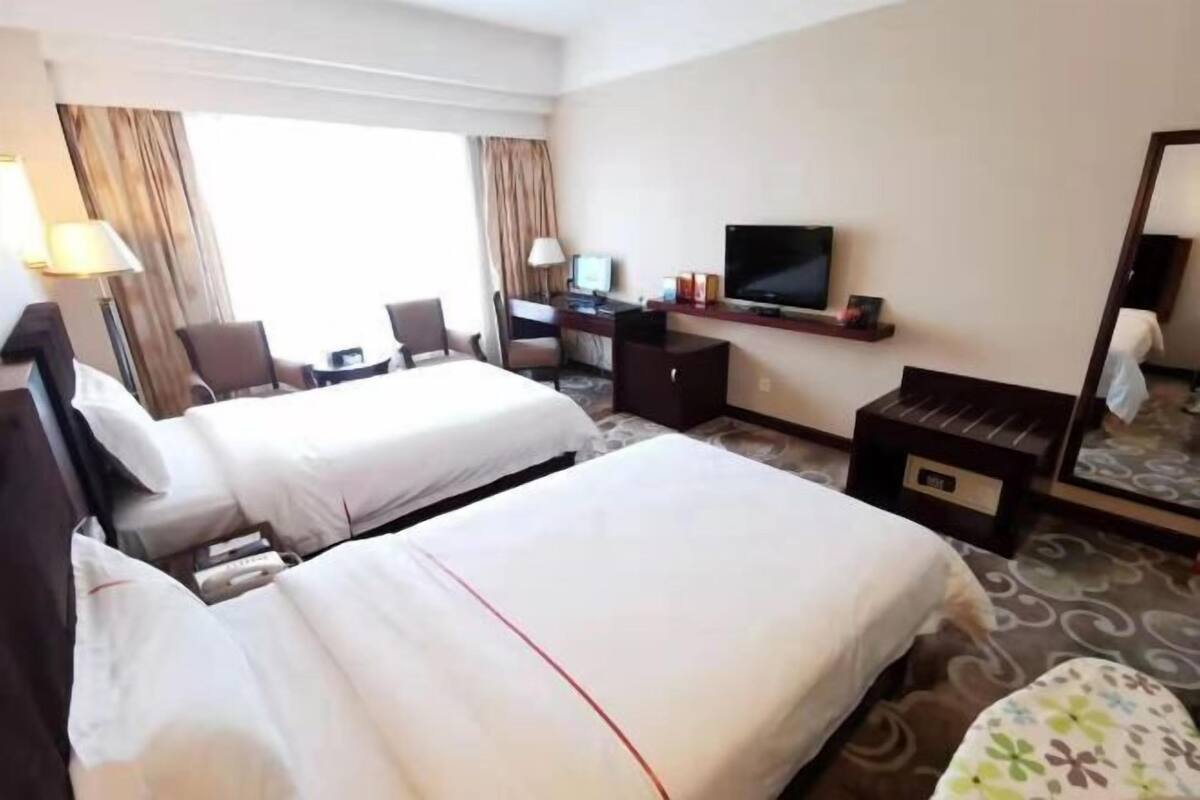 A hotel room with two beds, a desk with a computer, a TV, and a mirror.