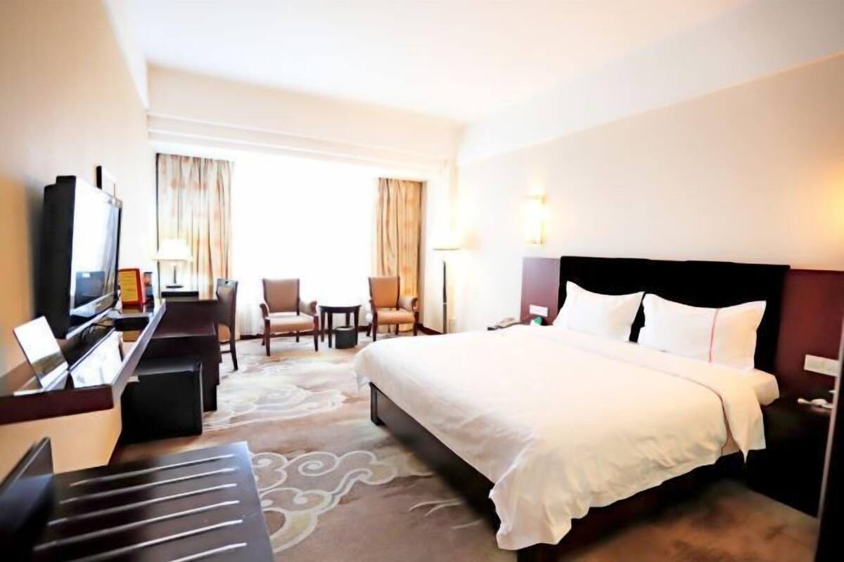A hotel room with a bed, a desk with a computer, a chair, a TV, and a lamp.