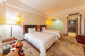 Une chambre d’hôtel avec deux lits, un bureau, une chaise, une lampe et un panier de fruits.