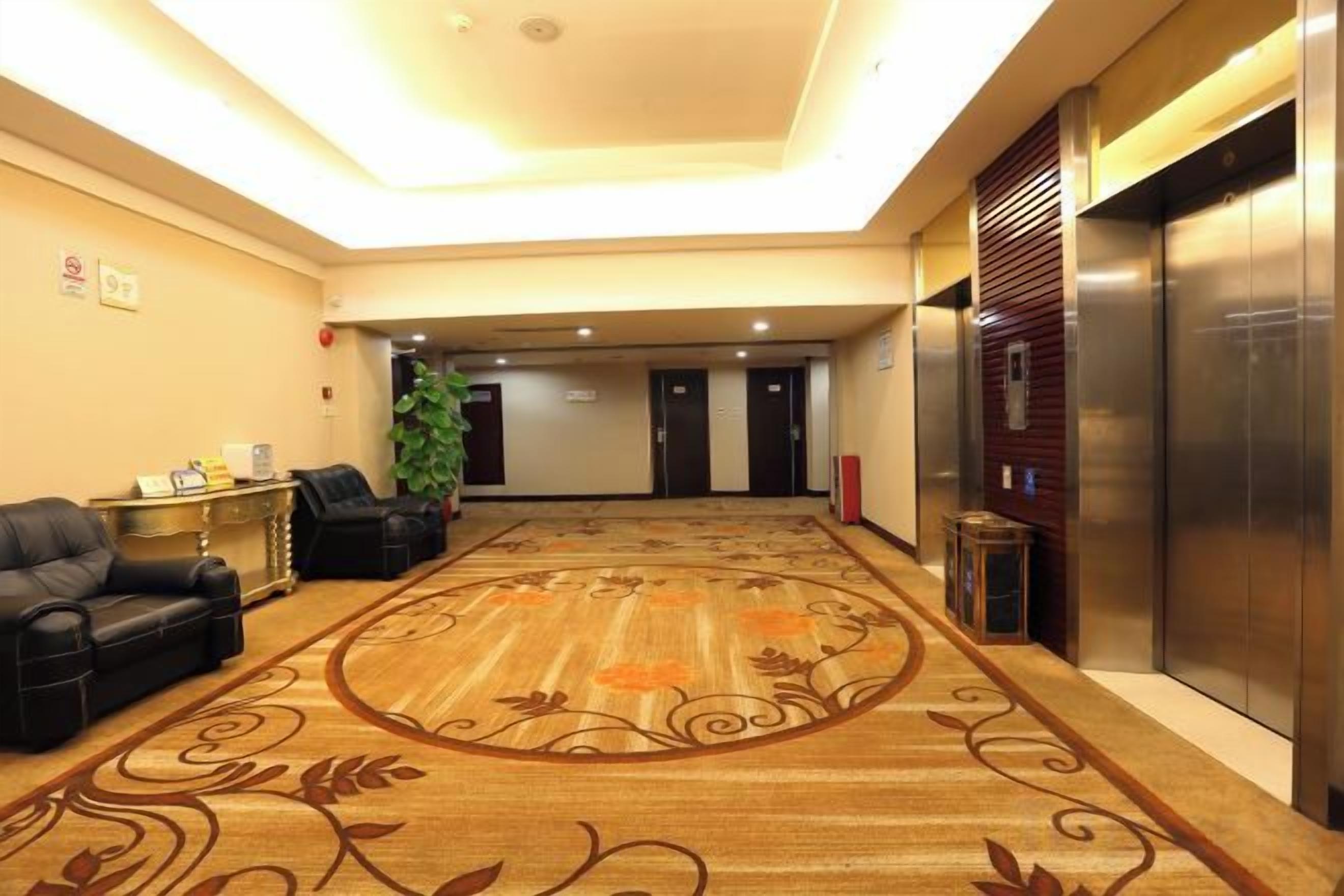 A hotel lobby with a carpeted floor, a reception desk, seating area, and elevators.