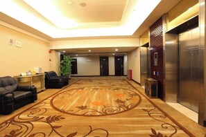 A hotel lobby with a carpeted floor, a reception desk, seating area, and elevators.