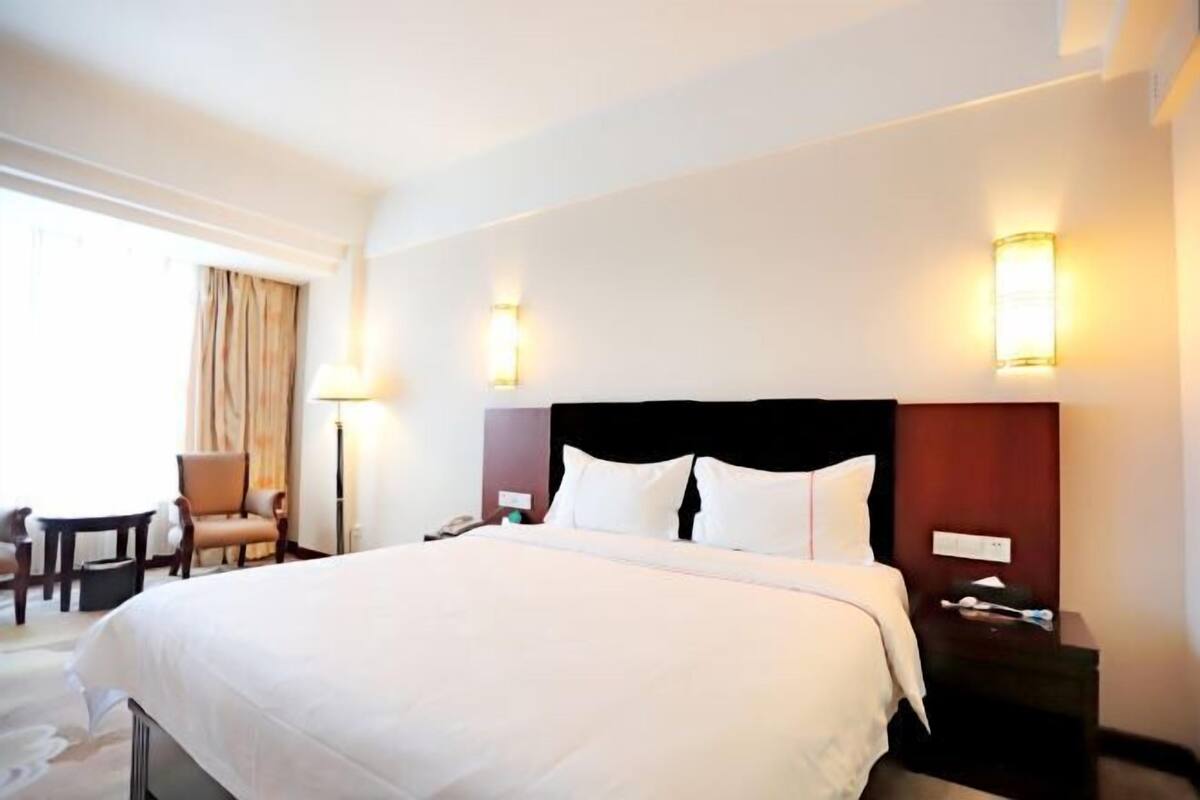 A hotel room with a large bed, bedside tables, a chair, and a lamp.