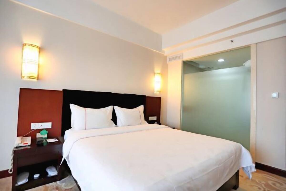 A hotel room with a large bed, bedside lamps, a nightstand, and a glass door leading to a bathroom.