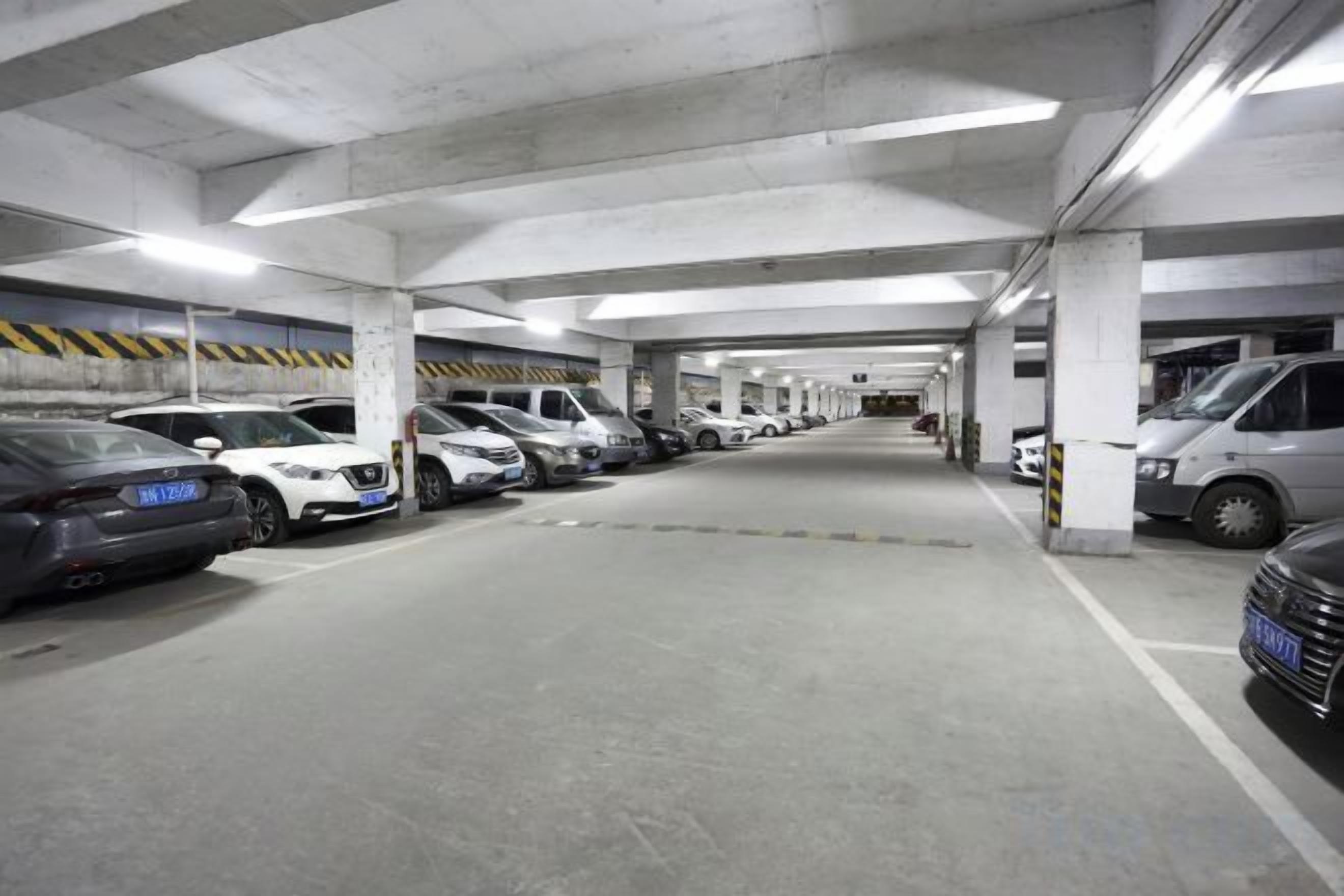 A multi-level underground parking garage with cars parked in rows, concrete pillars, and overhead lighting.