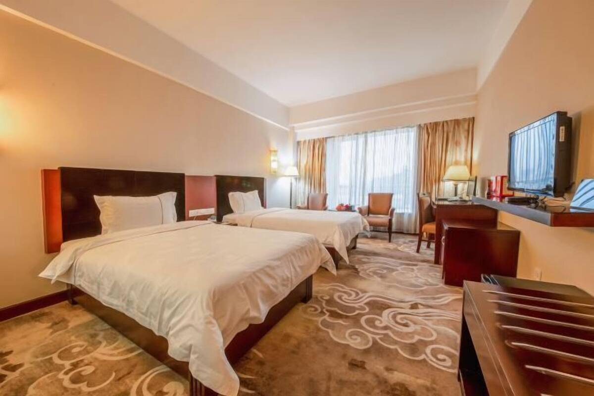 A hotel room with two beds, a desk, a chair, a television, and a carpet with a swirl pattern.