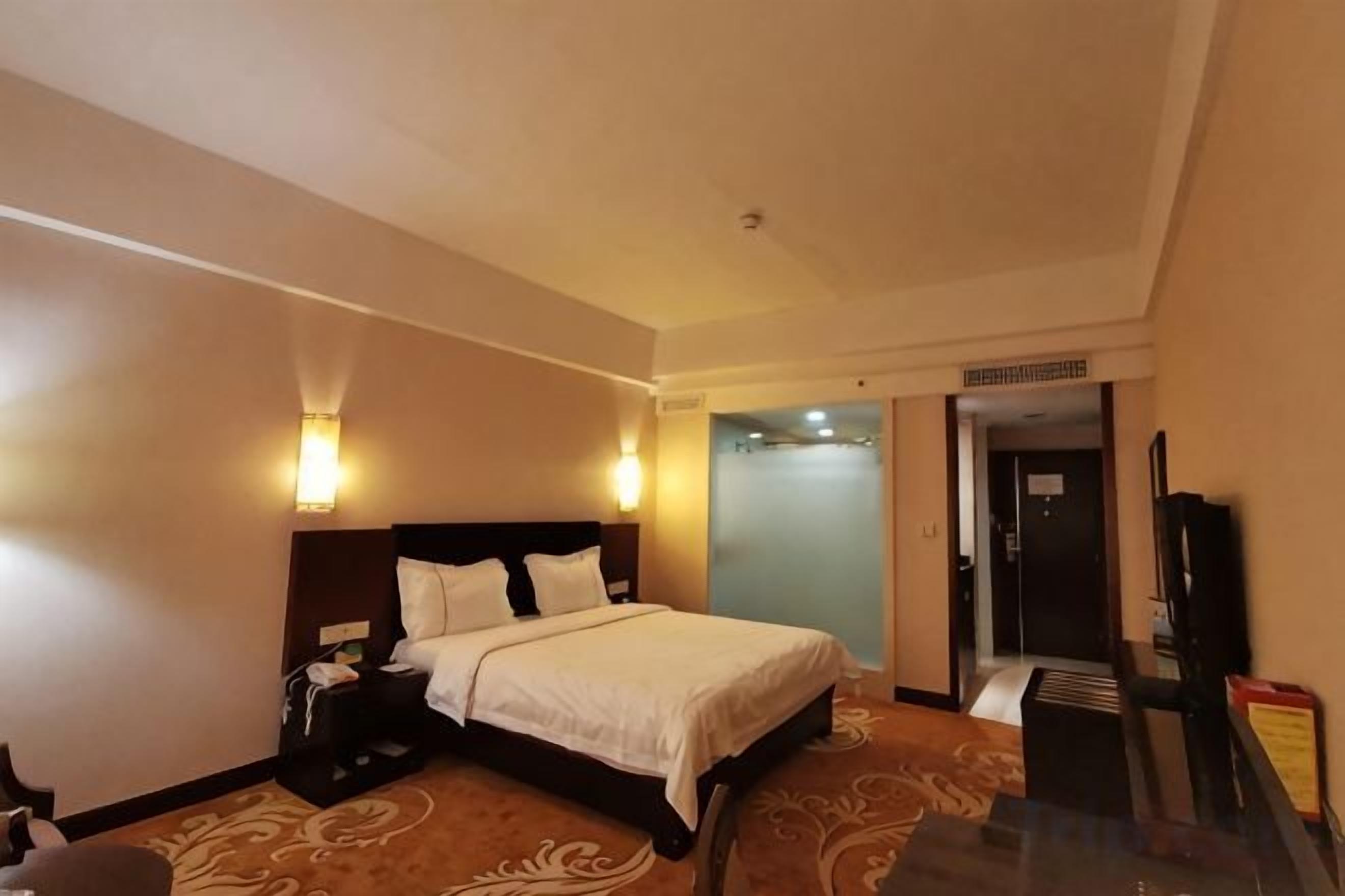 Una habitación de hotel con cama, mesita de noche, lámpara y televisor.