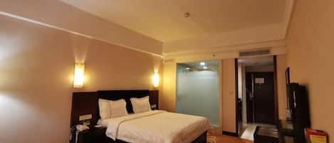 A hotel room with a bed, bedside table, lamp, and a television.