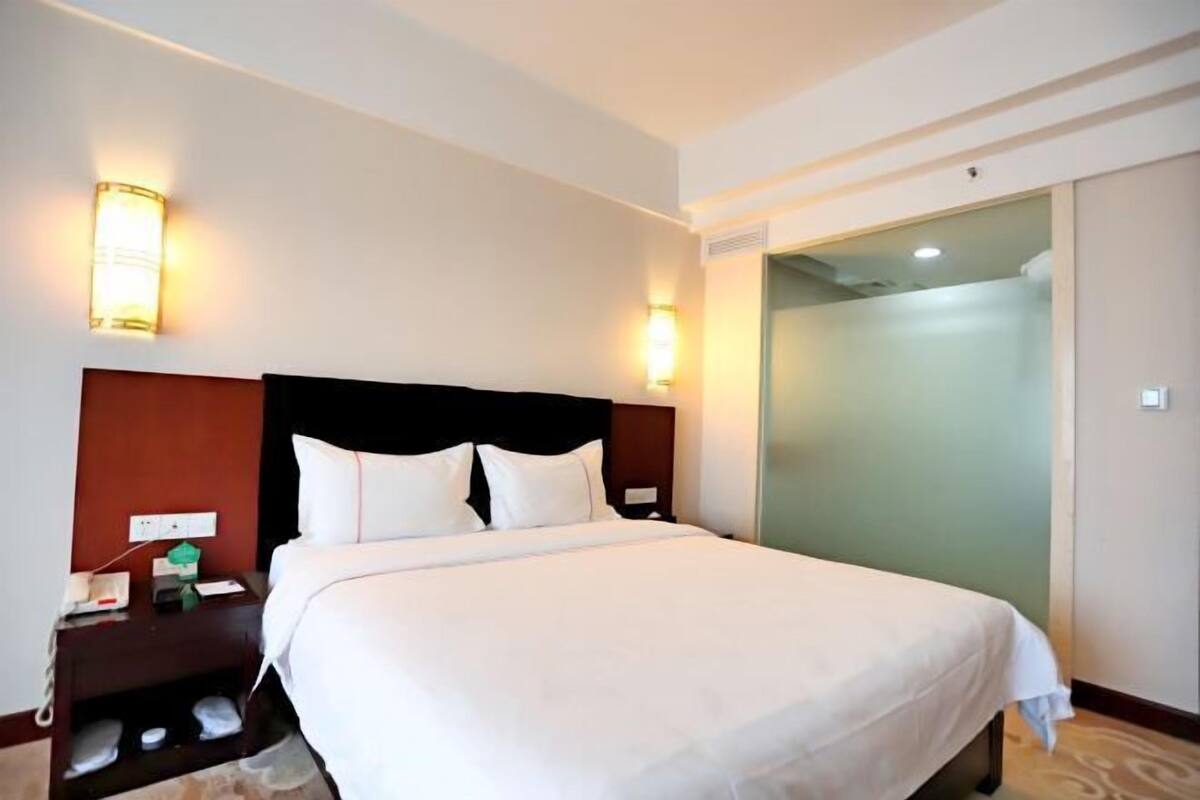 A hotel room with a bed, nightstand, wall-mounted lights, and a sliding door closet.