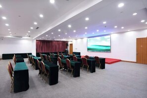A conference room with rows of tables and chairs, a large screen, and a red carpet. - May King Grand Hotel (Guangzhou)