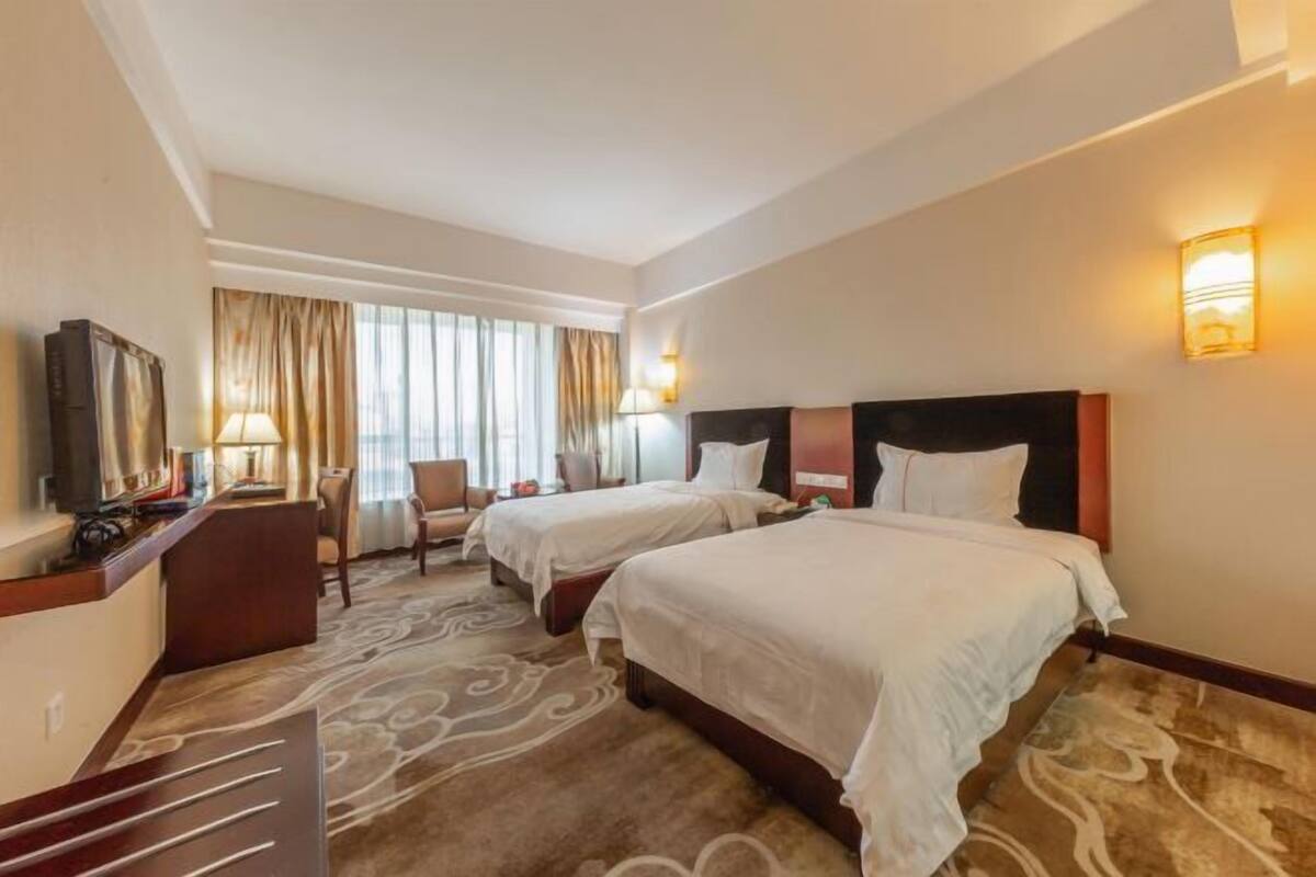 A hotel room with two beds, a desk, a chair, and a TV.