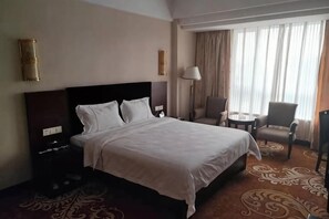 A hotel room with a large bed, a desk, a chair, and a view of the outdoors through the window.