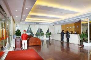 Un hall d’hôtel avec un comptoir d’accueil, un tapis rouge et une grande fenêtre avec des rideaux.