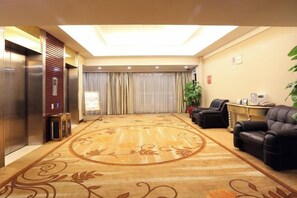A hotel lobby with a carpeted floor, a reception desk, a seating area with chairs, and an elevator. - May King Grand Hotel (Guangzhou)