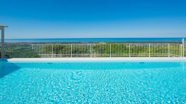Piscina azul cristalina con vista al océano y un paisaje urbano lejano.