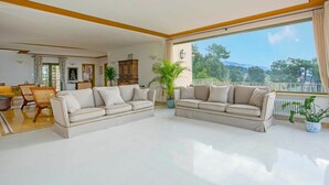 Un salón amplio con un ventanal grande que ofrece vistas al exterior. Cuenta con un sofá beige y una zona de comedor con mesa y sillas.
