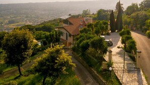Una villa en una ladera con entrada porticada, camino de acceso pavimentado y vistas del paisaje circundante.