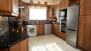 Eine moderne Küche mit Holzschränken, einem Edelstahlkühlschrank, einem Geschirrspüler, einer Waschmaschine und einer Kaffeemaschine.
