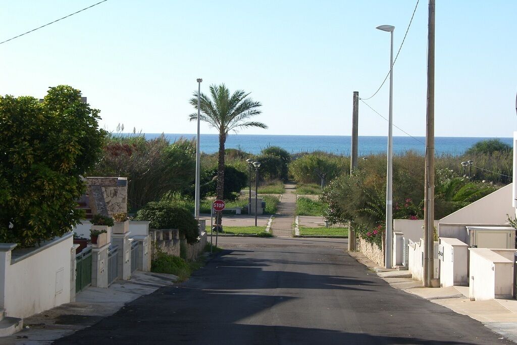 A residential street with houses, a stop sign, and a view of the sea.
