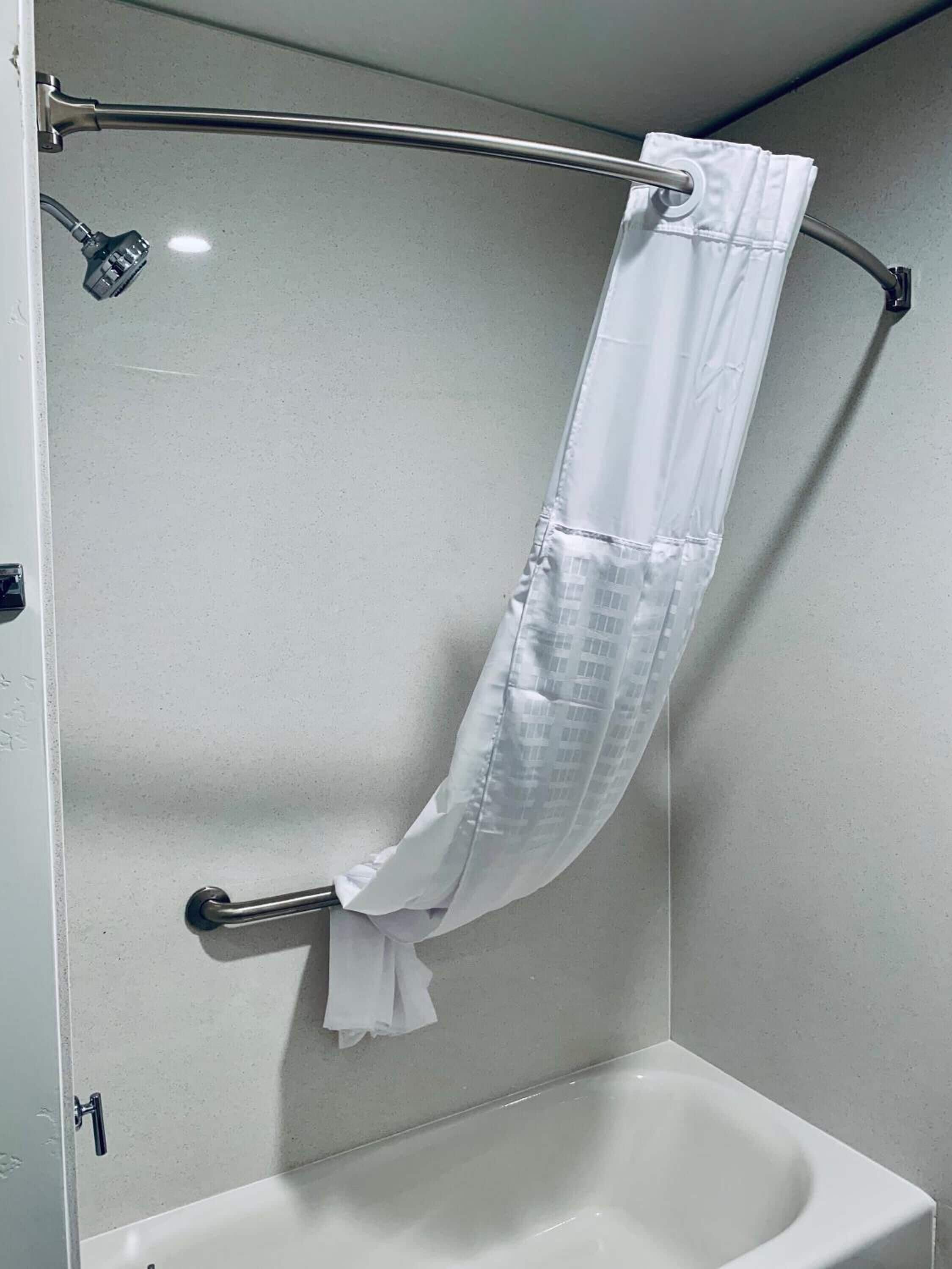 A shower area with a white shower curtain, a handheld showerhead, and a grab bar.