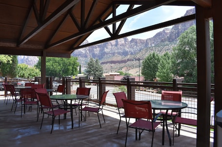 An outdoor patio with tables and chairs, a wooden ceiling, and a view of mountains.