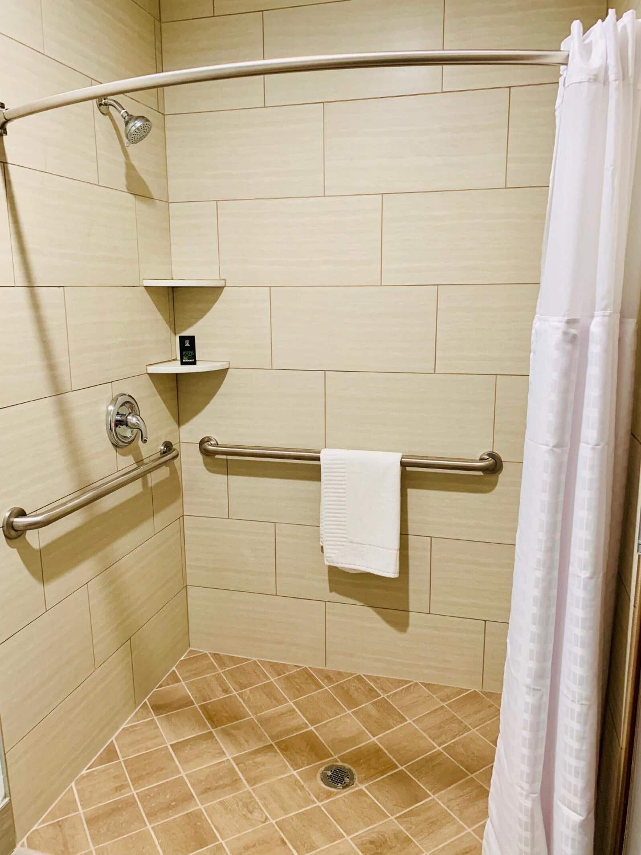 A shower area with a grab bar, a towel rack, and a shower curtain.