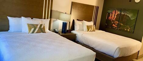 A hotel room with two beds, a nightstand with a lamp, a clock, and a painting on the wall.