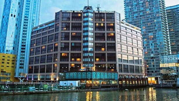 Un edificio en esquina con letreros que dicen "Britannia Hotels" y "The International", rodeado de edificios altos y una masa de agua.