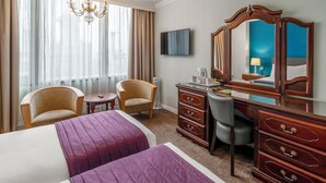 Habitación de hotel con dos camas, un escritorio, una silla, un aparador, un televisor y un amplio ventanal con cortinas.