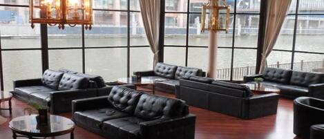 Un salón moderno con sofás de cuero, una mesa de centro de vidrio y vistas a un río a través de amplios ventanales.