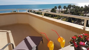A balcony with a view of the sea, a chair, two drinks, and a potted plant.