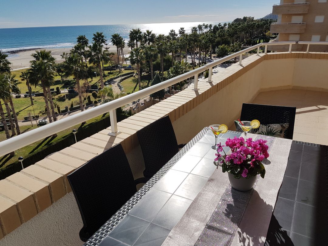 Un balcon avec une table et des chaises, donnant sur une plage et des palmiers.