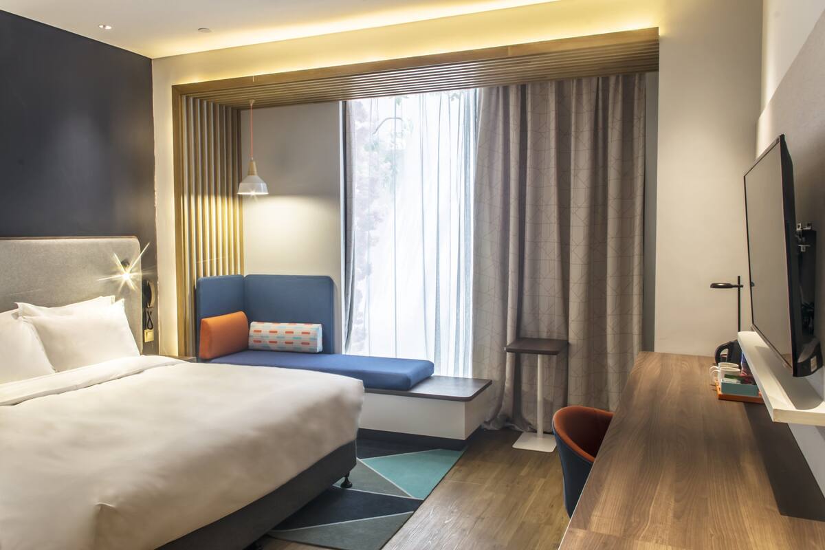 Ett modernt hotellrum med en stor säng, ett skrivbord, en stol och en TV.