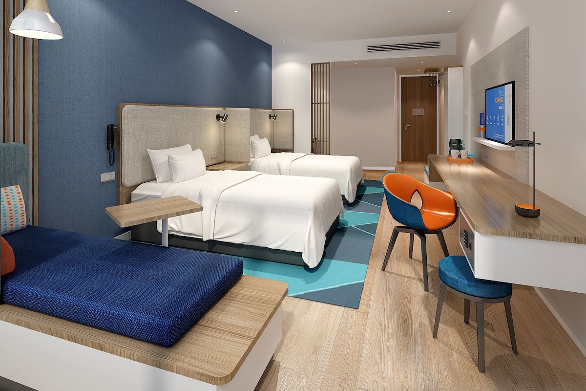 Ett modernt hotellrum med två sängar, ett skrivbord, en stol och en TV.