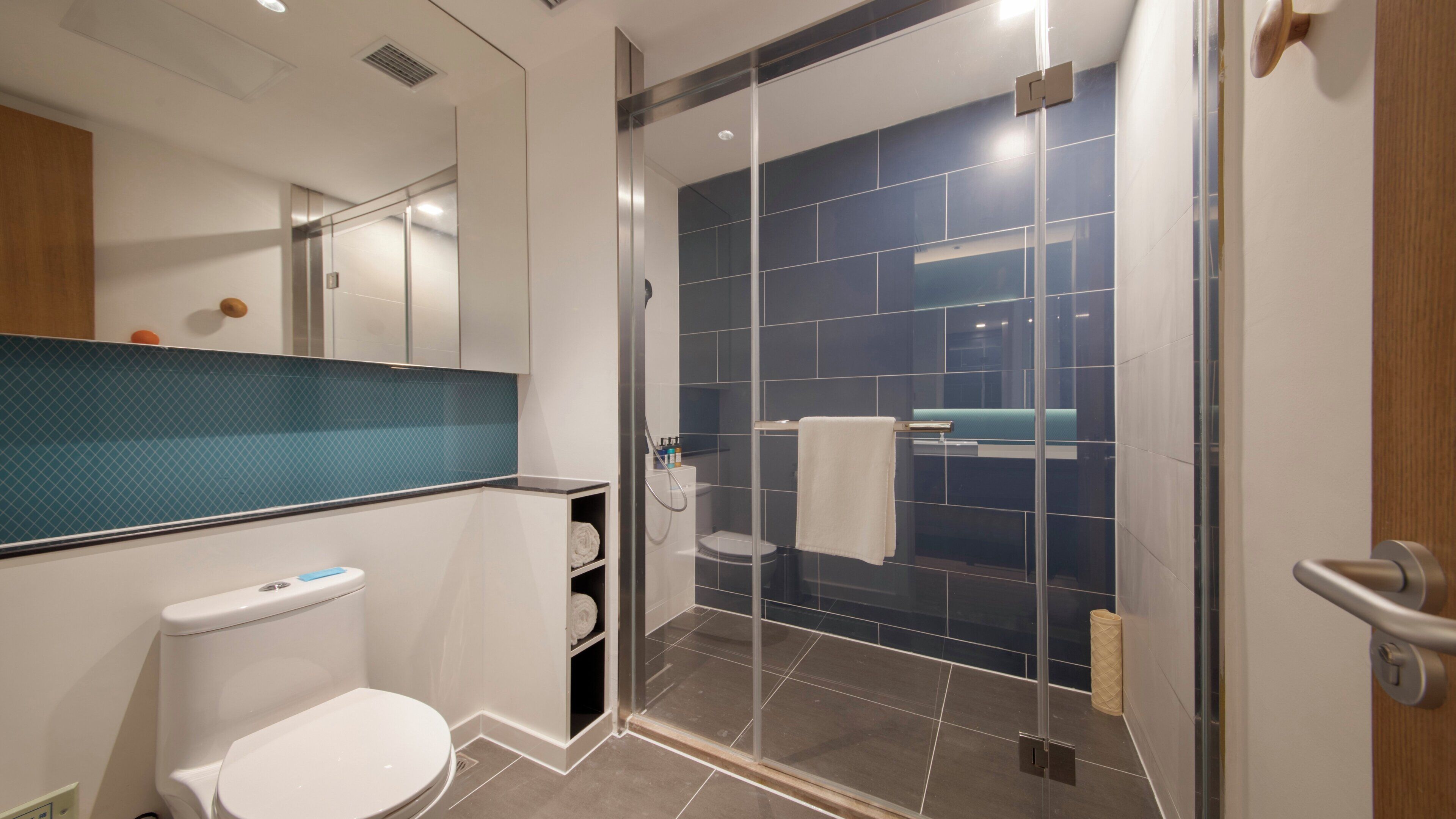 A modern bathroom with a toilet, a glass-enclosed shower, and a blue-tiled wall.