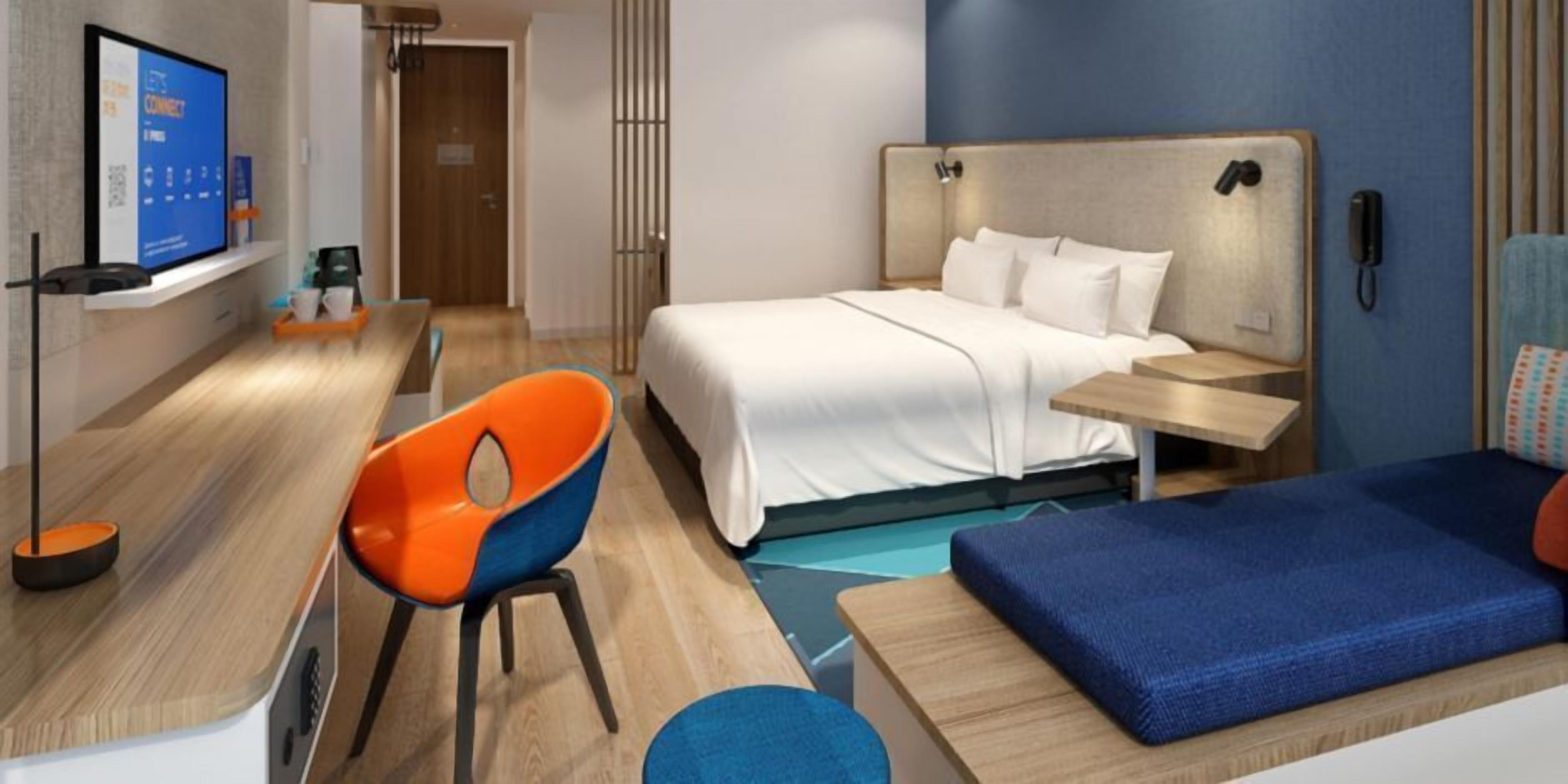 A modern hotel room with a bed, a desk, a chair, and a TV.