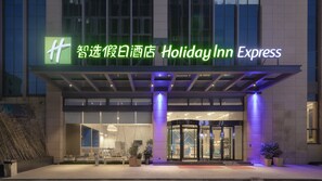 L’entrée d’un hôtel Holiday Inn Express, dotée d’une façade en verre et d’une enseigne au néon bien visible, présente un design moderne.