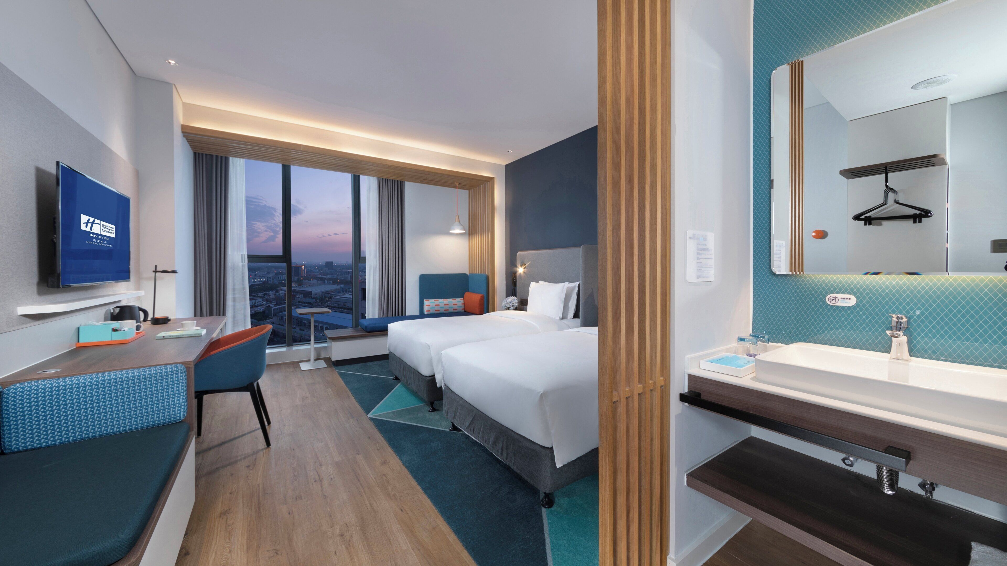 A hotel room with a bed, a desk, a chair, a TV, and a bathroom.