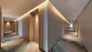 Un couloir d’hôtel avec des revêtements de sol en moquette, des portes et un éclairage encastré.