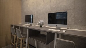 A modern office space with two Apple iMac computers on a long desk, a keyboard, mouse, and a vase with flowers. - Holiday Inn Express Nanjing Dongshan by IHG (Nanjing)