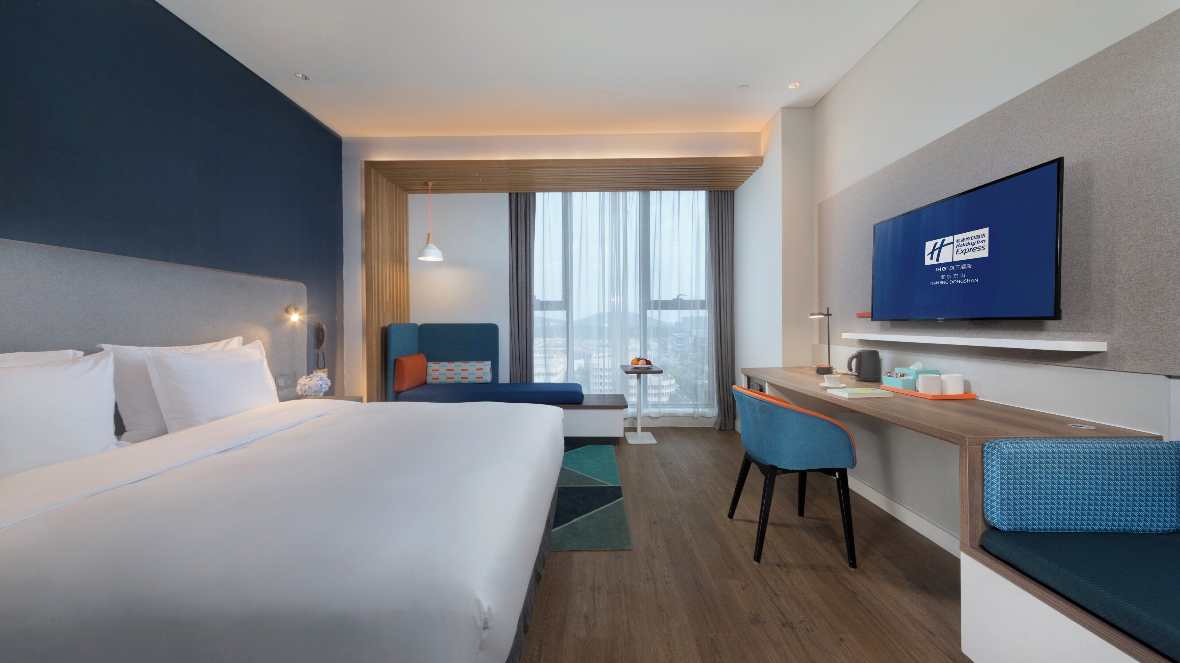 Ein Hotelzimmer mit Bett, Schreibtisch, Sessel, Fernseher und Blick auf die Stadt.
